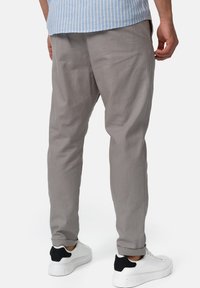 Jasnoszare spodnie o tapered fit, wykonane z miękkiego materiału, z delikatną teksturą i podwiniętymi mankietami, zestawione z białymi sneakerami.