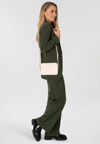 Blazer verde e pantaloni abbinati, abbinati a una piccola borsa a tracolla rosa. La borsa presenta hardware dorato e una finitura liscia e opaca.