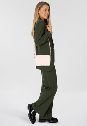 Blazer verde e pantaloni abbinati, abbinati a una piccola borsa a tracolla rosa. La borsa presenta hardware dorato e una finitura liscia e opaca.