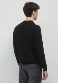 Schwarzer Pullover mit Kragen und gerippten Bündchen, aus Strickstoff. Wird mit grauen Jeans getragen und zeigt eine einfache, taillierte Silhouette.