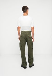 Pantalones cargo de pana verde oliva con múltiples bolsillos, diseño de pierna recta; combinados con una camiseta blanca y zapatos negros gruesos.