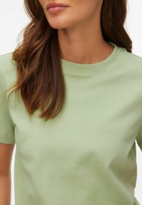 T-shirt z krótkim rękawem i okrągłym dekoltem w kolorze jasnozielonym, wykonana z bawełny o gładkiej fakturze i luźnym kroju. Subtelne przeszycia wokół linii szyi.