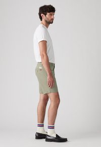 Șorturi bărbaști de un verde deschis cu buzunare, asortate cu șosete albe până la gleznă cu dungi roșii și albastre și mocasini negri. Tricou simplu alb.