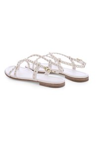 Weiße flache Sandalen mit breiten Riemen, verziert mit metallischen Nieten, ausgestattet mit einem Schnallenknöchelriemen und einer hellbraunen Sohle.
