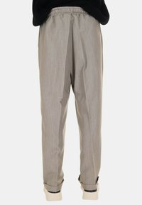 Pantaloni grigi chiari a taglio rilassato con cintura elastica, gambe affusolate e polsini a costine. Il tessuto ha una leggera texture con una leggera lucentezza.