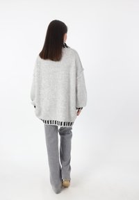 Overmatige lichtgrijze gebreide trui met zwarte gestreepte zoom, gecombineerd met grijze flared broek, gezien van achteren. Zachte textuur en relaxte pasvorm.