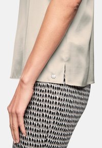 Light beige top with short sleeves and side slits, paired with patterned black and white fitted pants. Silver hardware accents on top.