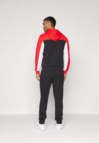 Chándal negro y rojo que incluye una sudadera con capucha y mangas en contraste, junto con unos joggers a juego. El material parece suave, con puños y dobladillo acanalados.