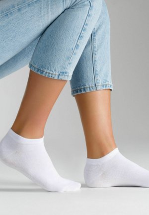 Calzini bianchi alla caviglia in cotone, con polsino a costine, texture liscia e design minimalista, abbinati a pantaloni corti in denim azzurro chiaro.