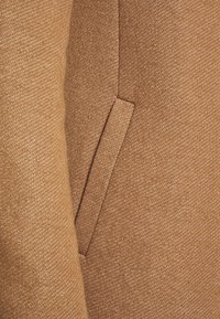 Brunt tekstureret stof med en skjult lomme og en subtil glans. Materialet har et blødt, vævet udseende og en rig farvedybde.