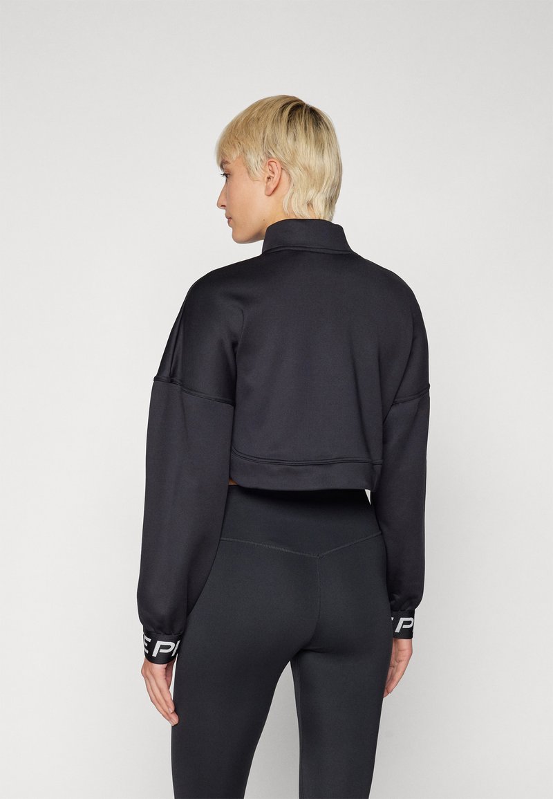 Schwarzer, cropped Sweatshirt mit hohem Kragen und überschnittenen Schultern. Verfügt über einen strukturierten Stoff und schwarze Leggings mit einem Logo-Band an den Bündchen.