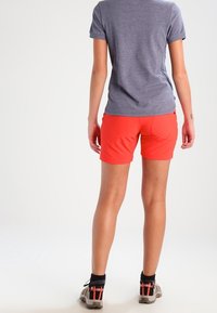 Shorts de sport rouges en tissu léger, associés à un t-shirt gris à manches courtes. Les chaussures visibles ont une semelle robuste.