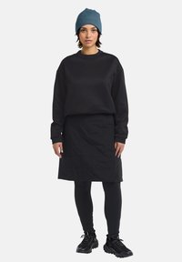 Felpa nera con una vestibilità ampia, abbinata a una gonna nera in tessuto trapuntato, leggings neri e sneakers nere. Viene indossato un berretto di maglia blu.