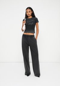 Zwarte cropped t-shirt met "Forever Hugo" in het grijs gedrukt, gecombineerd met donkere wijde broekspijpen en een kleine roze handtas.