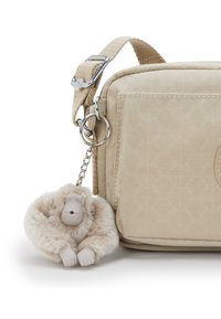 Beige crossbody bag with a textured surface and a decorative monkey keychain made from plush and plastic, featuring a light fur-like texture.