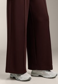 Szerokie spodnie w ciemnym burgundowym kolorze, gładka struktura, w połączeniu z jasnoszarymi sportowymi butami z meshu i gumowymi akcentami.