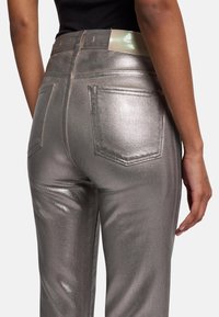 Metalen zilveren jeans met een aansluitend ontwerp, voorzien van twee achterzakken en een gladde textuur. De tailleband heeft een merklabel.