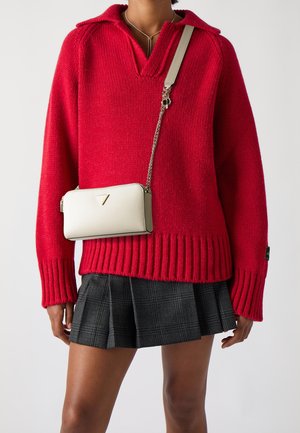 Suéter rojo de punto con escote en V y dobladillo acanalado, combinado con una falda de cuadros plisada negra y un bolso de cuero blanco bandolera.