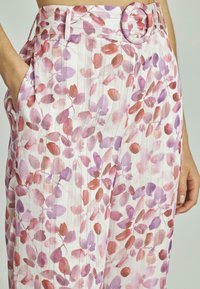Pantalons à motif floral avec une base rose clair, ornés de designs de feuilles rouges et violettes, taille ajustée avec une ceinture ronde, et poches latérales.
