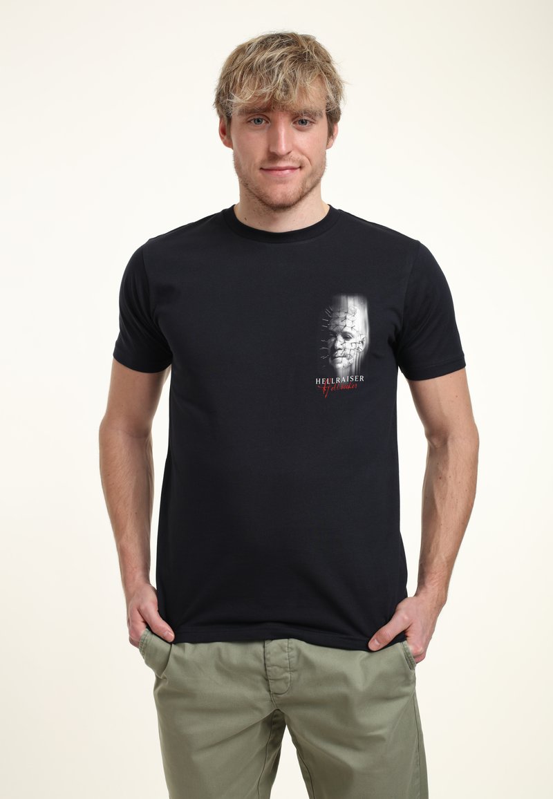 Czarna koszulka z krótkim rękawem z graficznym nadrukiem twarzy w górnym lewym rogu, z napisem "HELLRAISER" na czerwono. Gładki materiał.