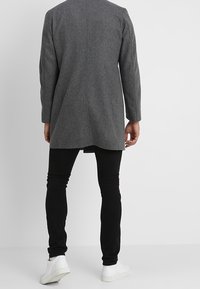 Abrigo gris de mezcla de lana con un diseño simple, mangas largas y corte recto, llevado sobre pantalones negros ajustados y zapatillas blancas.