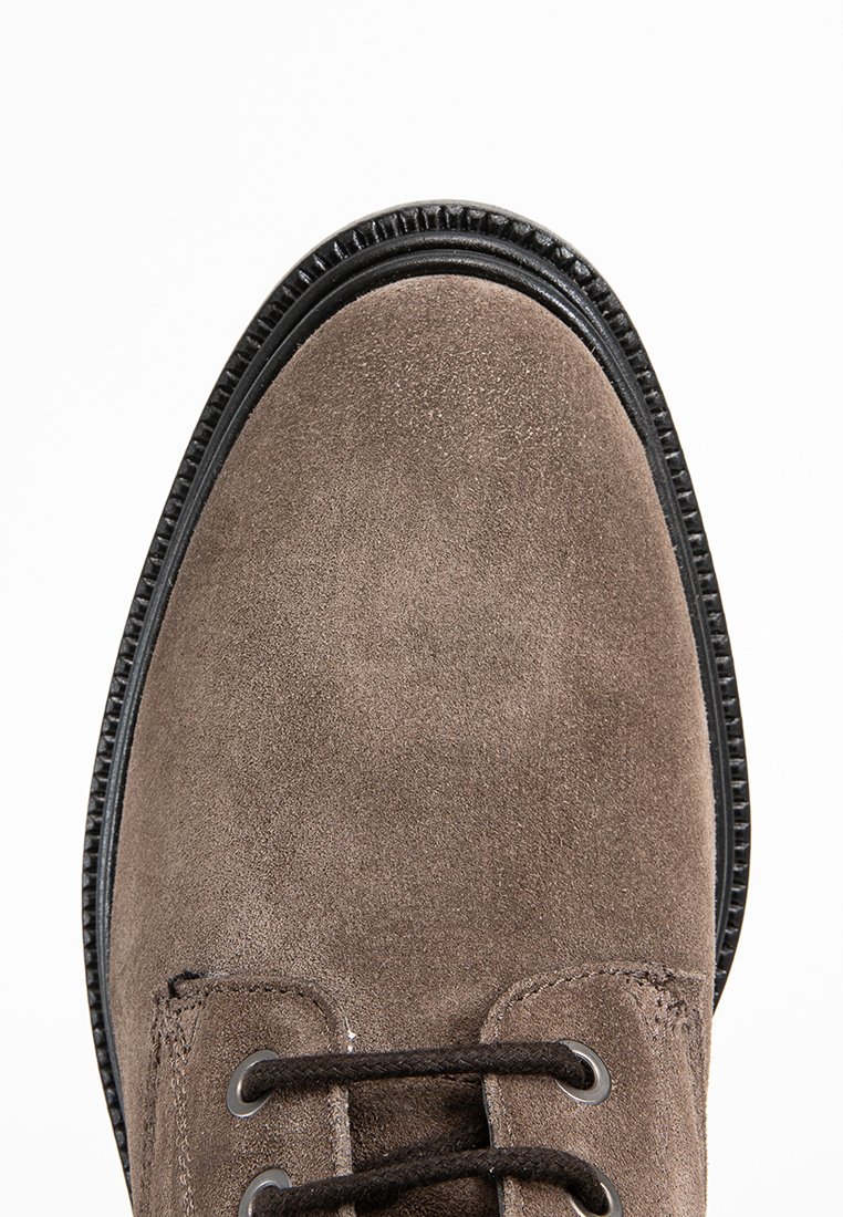 Brauner Wildlederschuh mit schwarzer Schnürung und schwarz genähtem Sohlenrand, von oben auf einem weißen Hintergrund gezeigt.