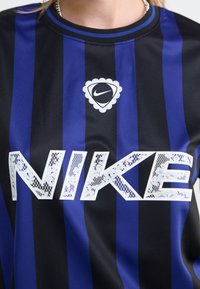 Jersey de Nike a rayas negras y azules con un gran logo "NIKE" texturizado en blanco y un emblema redondo de Nike en el pecho.