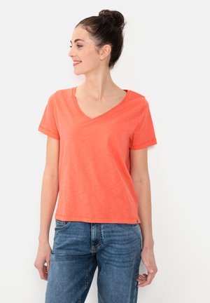 T-shirt corail en V fabriqué en tissu doux, avec des manches courtes et une coupe décontractée. Associé à un jean en denim bleu.