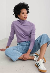 Långärmad lila polotröja paired med ljusblå vida denim culotter och vita sneakers med gröna accenter. Avslappnad outfit.