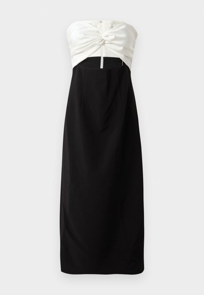 Bespdė su petnešomis su kreminiu satino liemeniu, kuriame yra mazgo detalė, derinama su juoda, lygaus audinio sijonu ir užmaskuotu užpakaliniu užtrauktuku.