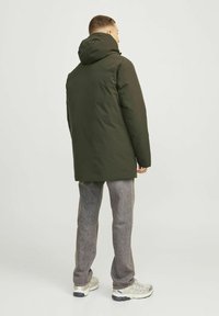 Grøn, isoleret parka med hætte, der har en glat overflade og en lige pasform. Båret over lysegrå, strukturerede bukser og sneakers.