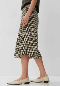 Gonna plissettata con motivo geometrico in marrone, crema e giallo, caratterizzata da un taglio di lunghezza media. Indossata con scarpe flat color crema.