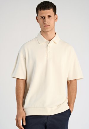 Polo a maniche corte in crema, realizzato in tessuto morbido. Presenta un colletto tradizionale e una chiusura a tre bottoni, con una vestibilità rilassata.