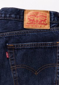 Poche arrière d'un jean Levi's bleu foncé avec des coutures orange et une étiquette en cuir beige Levi Strauss & Co. cousue à la taille.