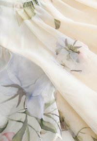 Durchsichtiger Stoff mit floralem Muster in sanften Pastellfarben. Das Design umfasst ein strukturiertes Netzgewebe und einen elastischen Bund.