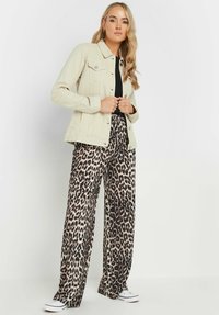 Beige denimjacka med krage, framknappning och två bröstfickor, i kombination med svarta och krämfärgade leopardmönstrade vida byxor.