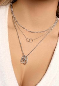 Colliers en argent à trois couches avec des chaînes torsadées, un pendentif rond et un design de formes ovales entrelacées. Texture métallique lisse.