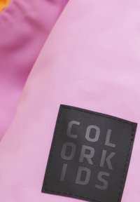 Rosa tyg med en texturerad yta, med en svart rektangulär patch med präglad text "COLOR KIDS."