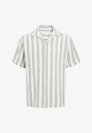 Dospievajúci nosiaci bordovú čiapku, bielu košeľu na gombíky a šortky s vertikálnymi čiernymi pruhmi, biele ponožky a tenisky, stojaci a usmievajúci sa.