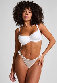 Witte kanten lingerie set met een volledig gevoerde bh en een doorschijnende string met polkadot en kanten accenten. Soepele textuur en bloemrijke details.