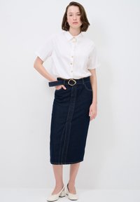 Camicia bianca a maniche corte con bottoni dorati abbinata a una gonna midi in denim scuro con una cucitura frontale e una cintura con fibbia dorata.