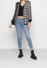 Blazer a cuadros en blanco y negro sobre un top corto negro de canalé, combinado con unos vaqueros ajustados azul claro y botas gruesas negras con cordones.