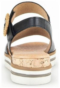 Sandale noire avec semelle en liège, deux brides courbes, un détail tissé rond et une semelle superposée avec des accents blancs, marron et gris.