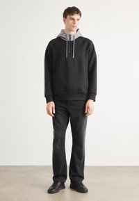 Hanorac negru cu captuseala gri, dotat cu siret si buzunar frontal, asortat cu blugi inchisi la culoare si pantofi negri. Design simplu.
