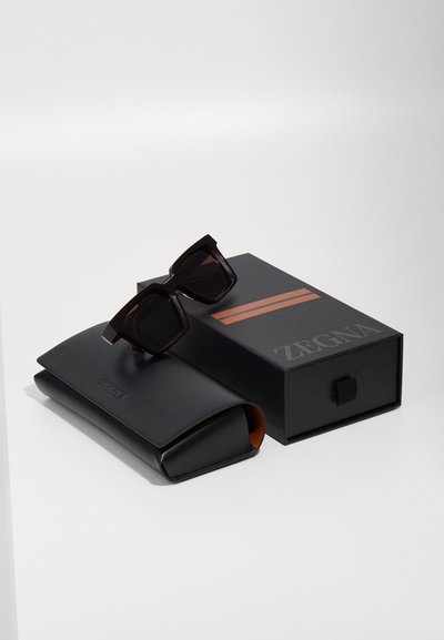 Black square sunglasses on a black case with orange interior, accompanied by a black box featuring orange stripes and the Zegna logo.