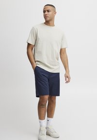 Light beige cotton t-shirt, crew neckline; navy shorts; white sneakers; medium-length, straight cut. Simple, casual outfit with minimal design.