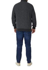 Dark gray knit sweater with a textured pattern, rounded collar, and ribbed cuffs, paired with blue jeans and light-colored shoes.
