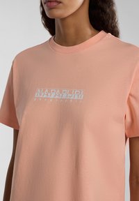 Helles Pfirsichfarbene Kurzarm-T-Shirt aus weichem Stoff, mit einem weißen Logoaufdruck, auf dem "NAPAPIJRI" und "geographic" darunter steht.