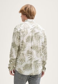 Camicia a maniche lunghe in tessuto leggero con motivo di foglie di palma verdi su sfondo bianco; presenta colletto e polsini abbottonati.