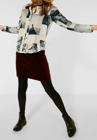 Camicetta a quadri bianca e nera con grafiche di montagne; abbinata a una gonna di velluto a coste bordeaux e stivaletti neri.